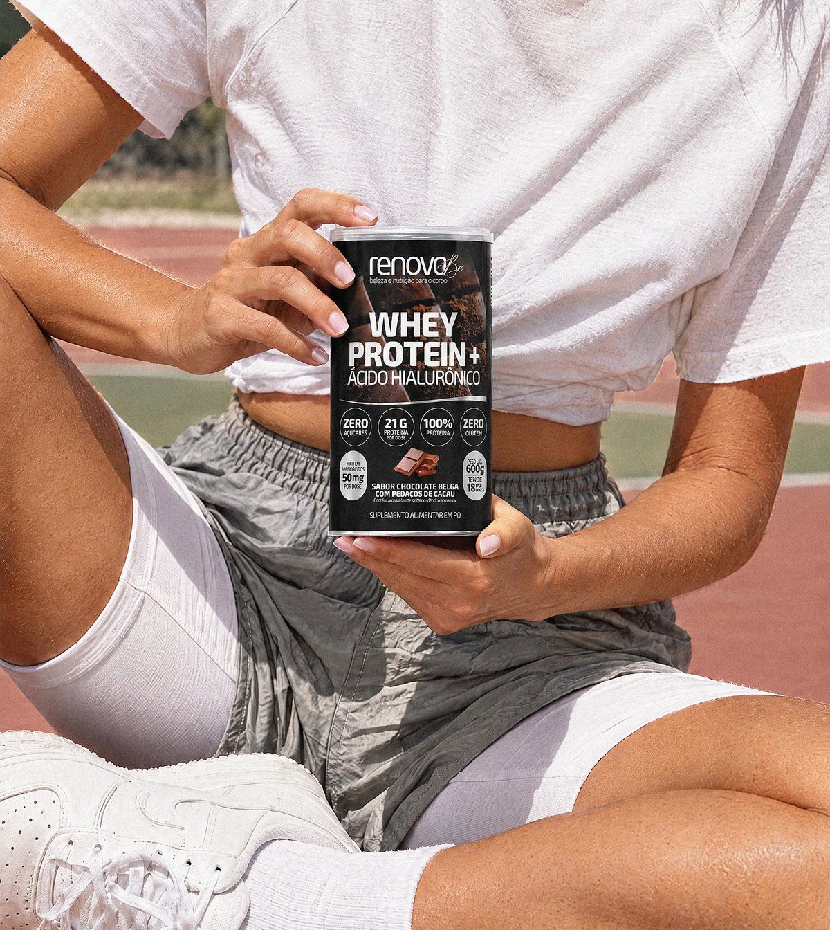 Mulher sentada na quadra segurando o pote do Whey Protein sabor chocolate belga